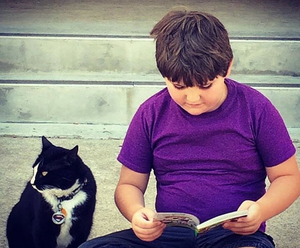 A Student with autism sits outside the school reading next to a cat