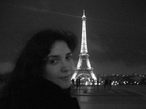A black and white image of the author in Paris with the Eiffel tower glowing behind her during her time as an au pair