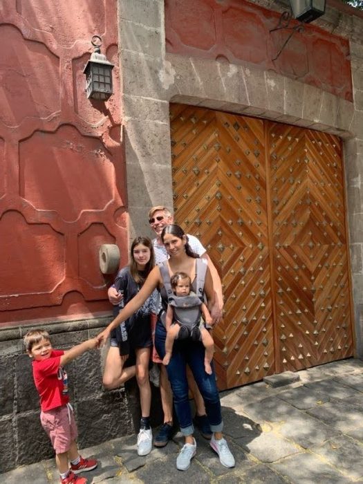 The author's family poses in front of beautiful doors in the Coyoacan neighborhood in Mexico City. Her toddler son tries to pull them along illustrating the challenges of international family trips.
