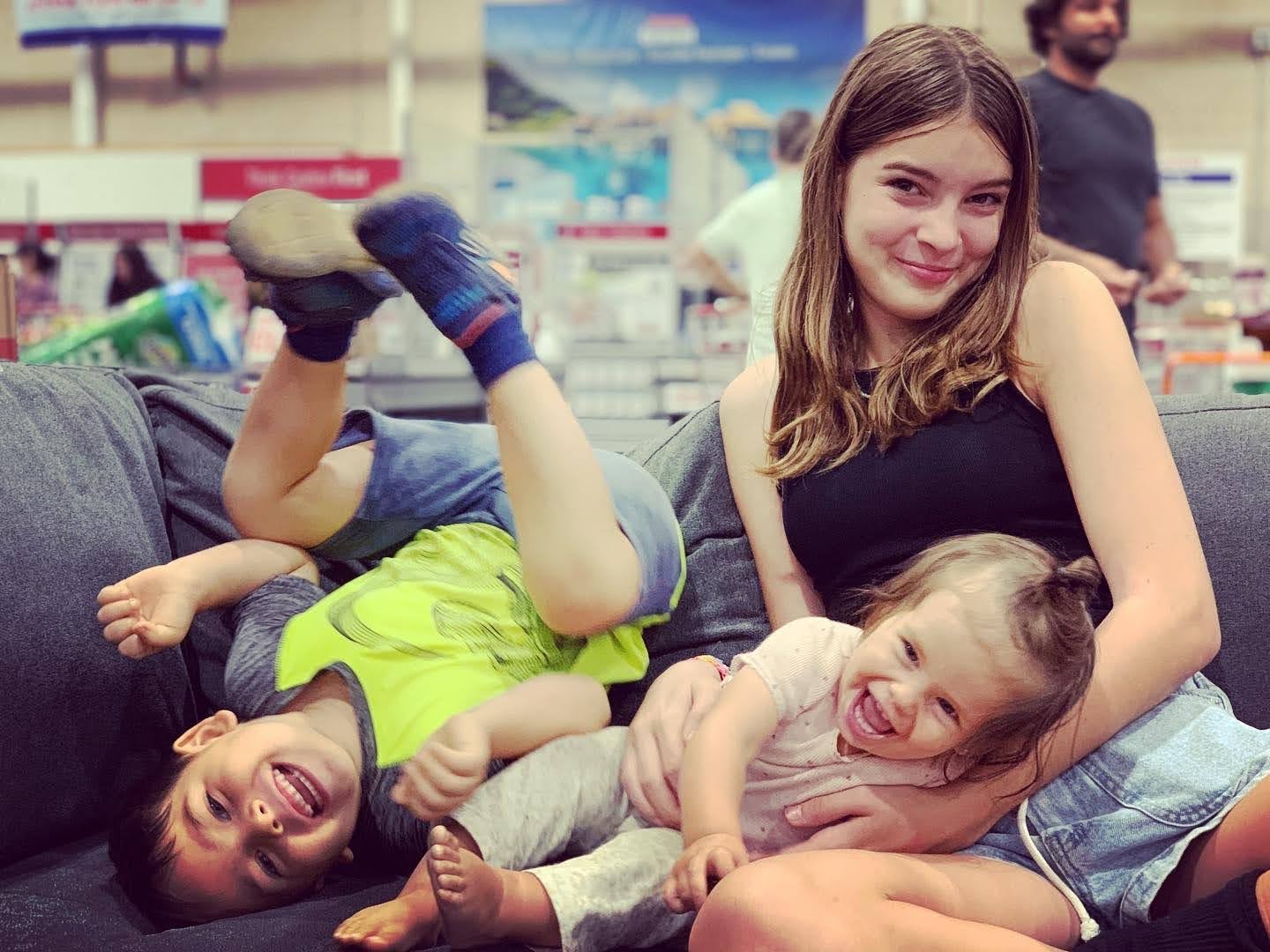 Three children pose on a couch in a Costco warehouse.