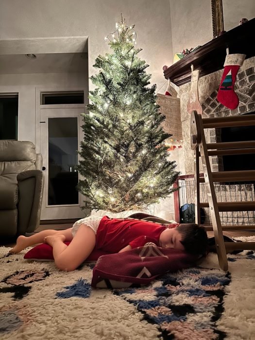 The author's son sleeps at the foot of their Christmas tree.