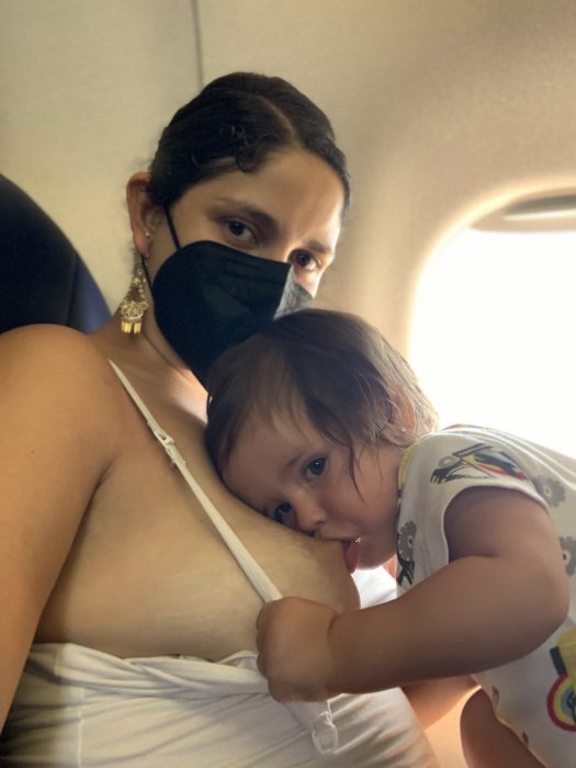 The author Angela De Hoyos Hart nurses her baby on an airplane, wearing a KN-95 mask during the end of COVID-19 protocols