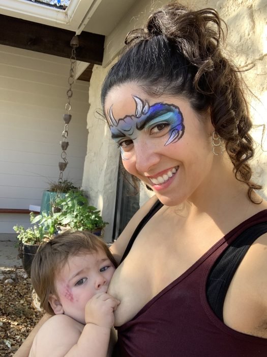 The author Angela De Hoyos Hart nurses her son after his 1 year old birthday party, both of them decorated in dragon facepaint.